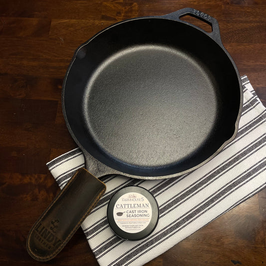 Made in USA cast iron skillet kit: Lodge 10.25” pre-seasoned skillet, Cattleman tallow seasoning tin, and Lindy leather handle cover on rustic wood surface
