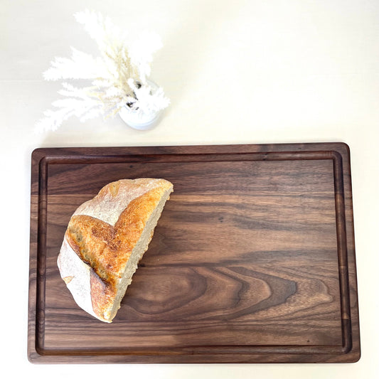 Premium black walnut cutting board with fresh sourdough bread and grapes – Handcrafted in USA by Refine Kitchenware
