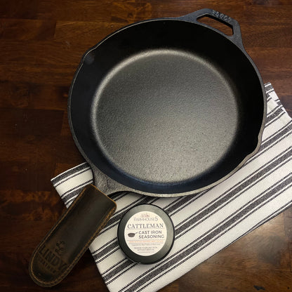 Made in USA cast iron skillet kit: Lodge 10.25” pre-seasoned skillet, Cattleman tallow seasoning tin, and Lindy leather handle cover on rustic wood surface