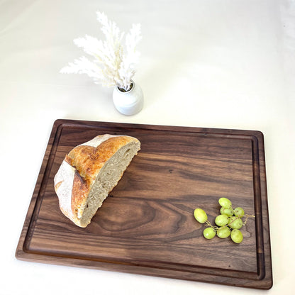 Premium black walnut cutting board with fresh sourdough bread and grapes – Handcrafted in USA by Refine Kitchenware